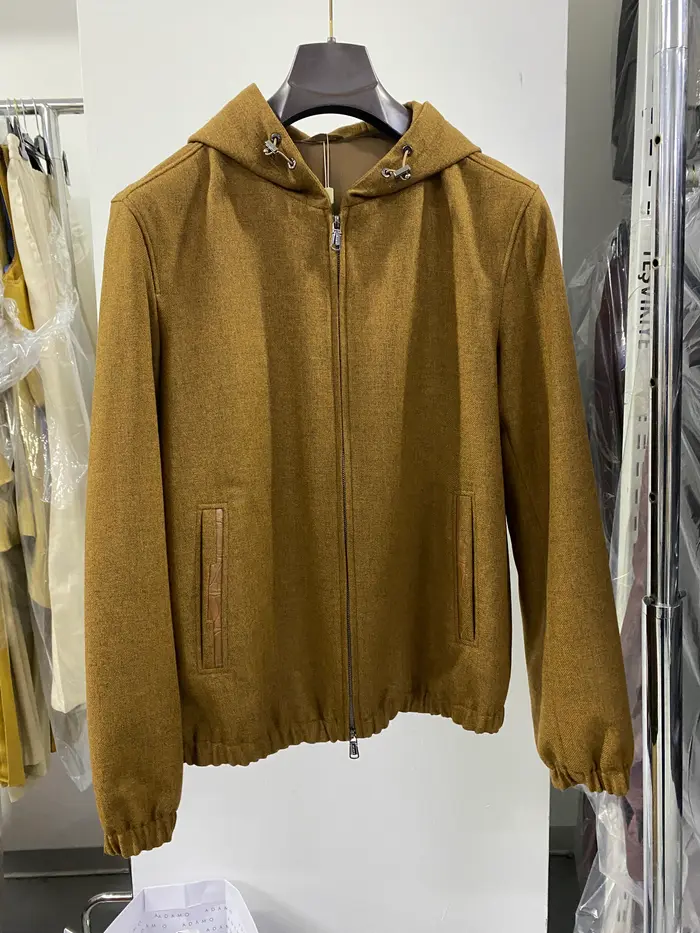 A camel wool hooded jacket on a hanger in a stockroom, photographed on a phone